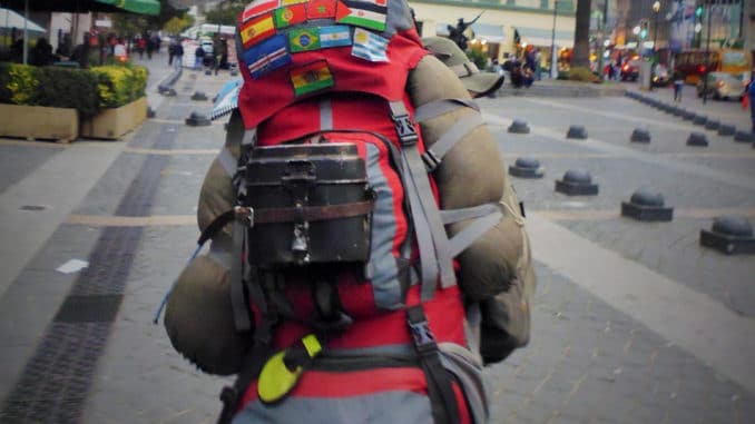 tourist heavily laden down with things strapped to backpack